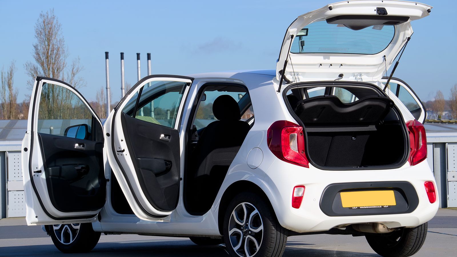 A white compact car with open doors and trunk, photographed in an urban outdoor setting.