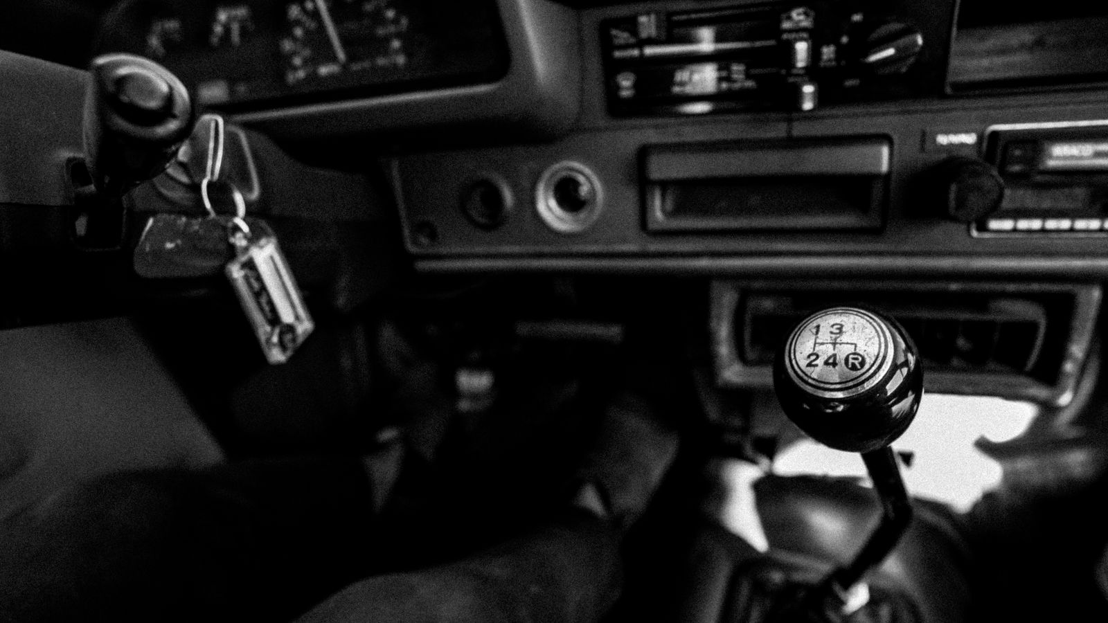 Black and white photo showcasing a vintage car interior with a manual gearshift and dashboard.
