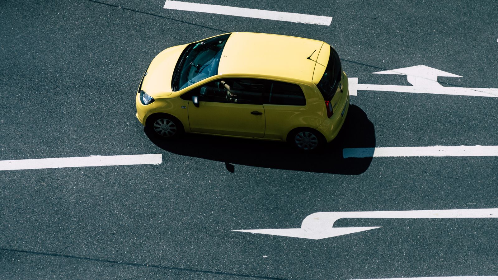 Aerial view of a yellow car on a road with directional arrows, highlighting urban transport.