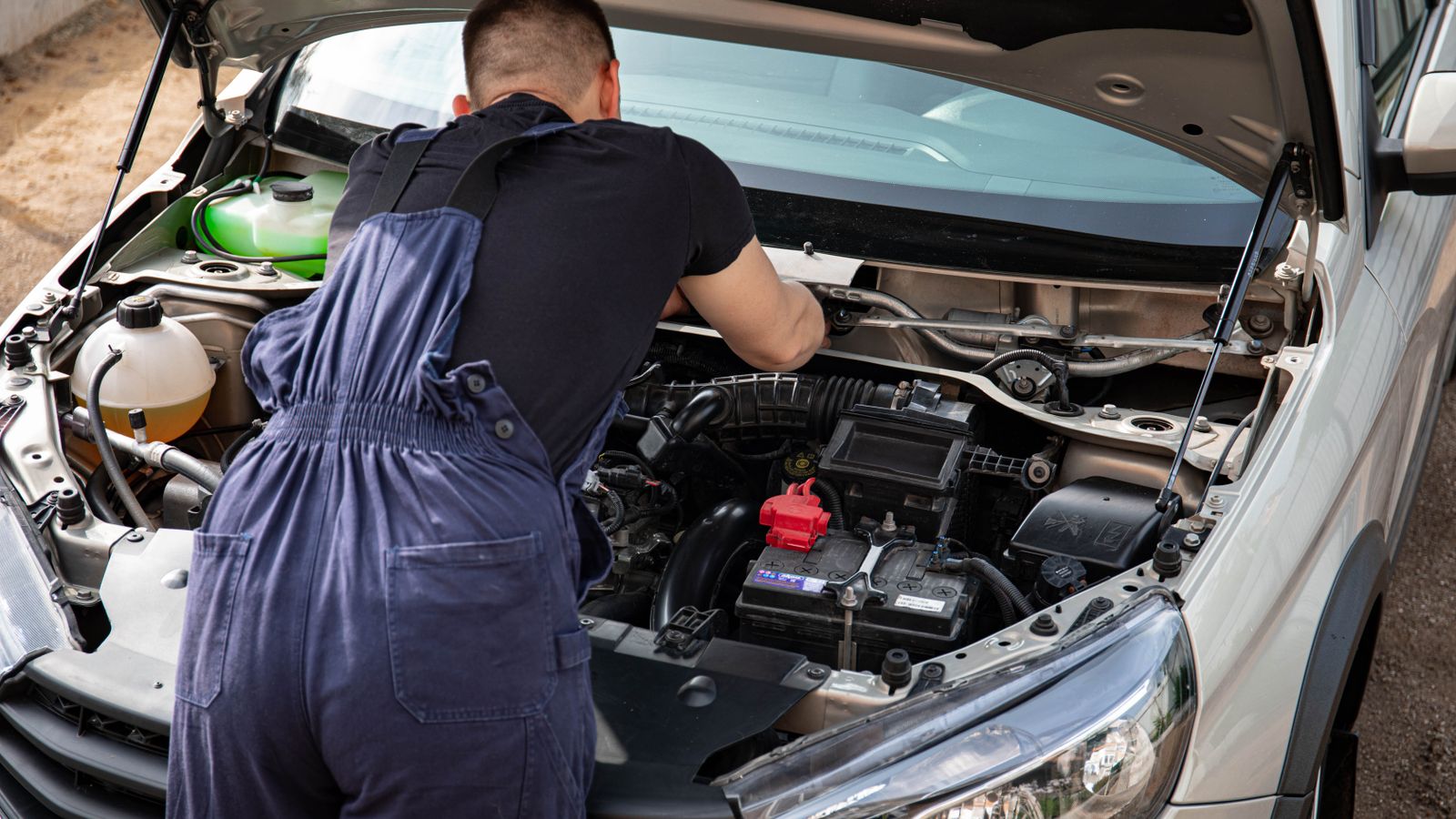 Close-up of mechanic repairing a car engine. Outdoor setting during the day.