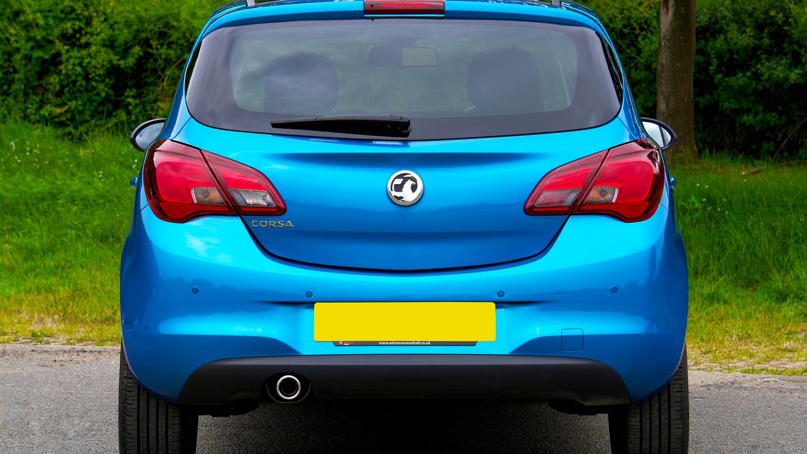 A blue hatchback car parked outdoors against a green background, showcasing its rear design.