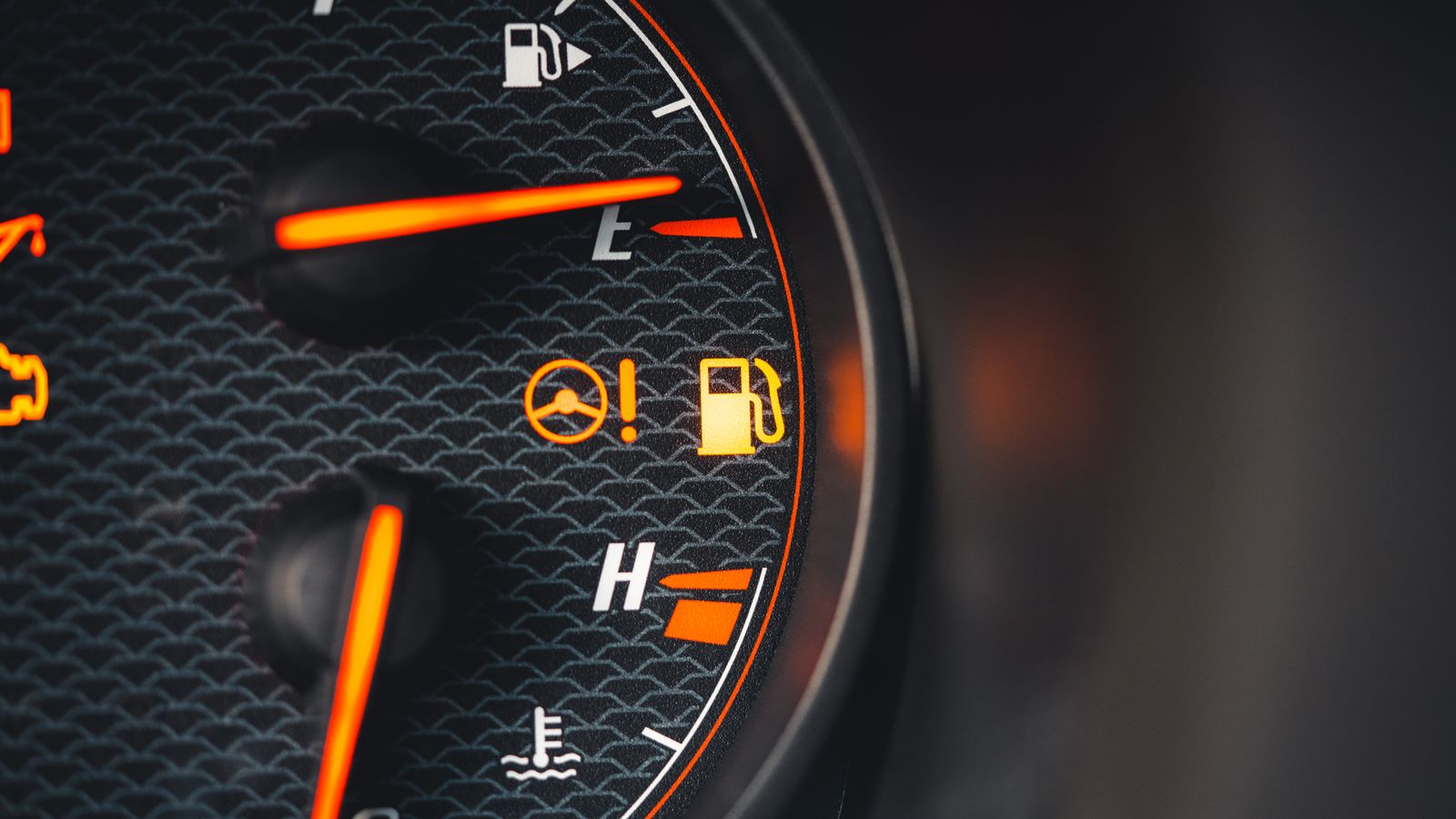Detailed view of a car dashboard showing fuel and temperature indicators with glowing pictographs.
