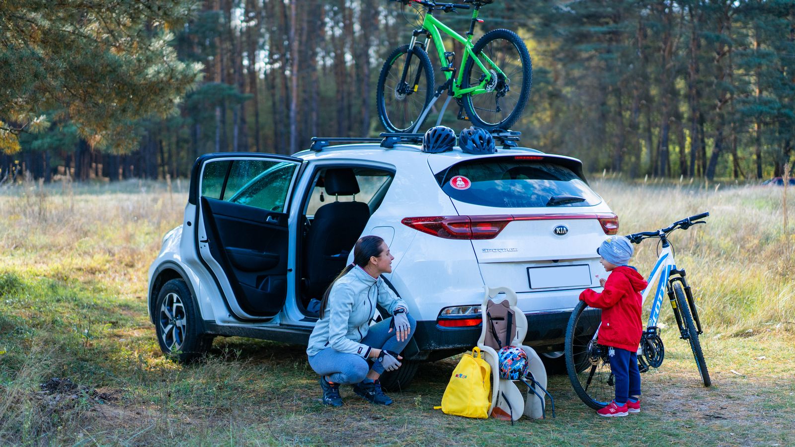 Mother and child preparing for a cycling adventure in a scenic park with bikes and a parked car.