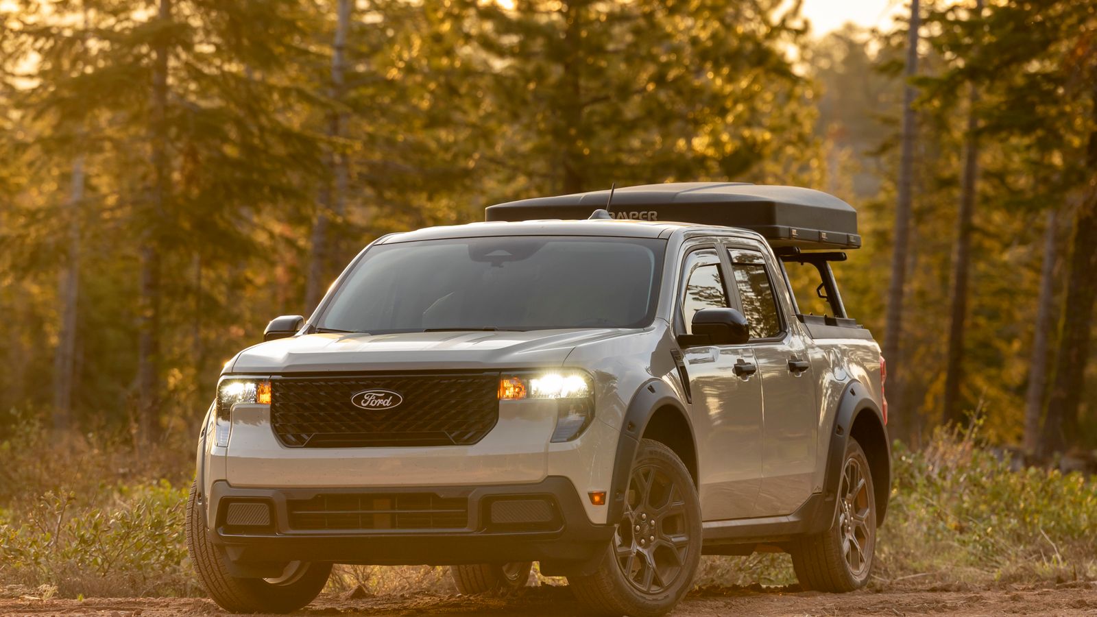 A sleek pickup truck parked on a dirt road with a forest backdrop at sunset. Adventure-ready.