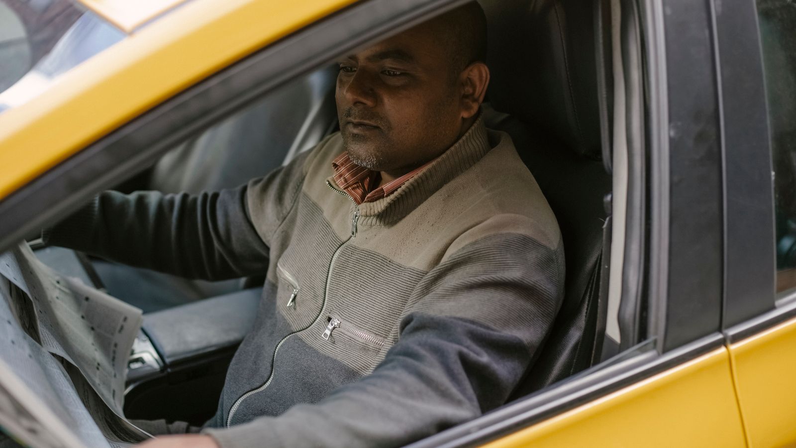 Ethnic male driver reading daily newspaper with interest while sitting in car and having break